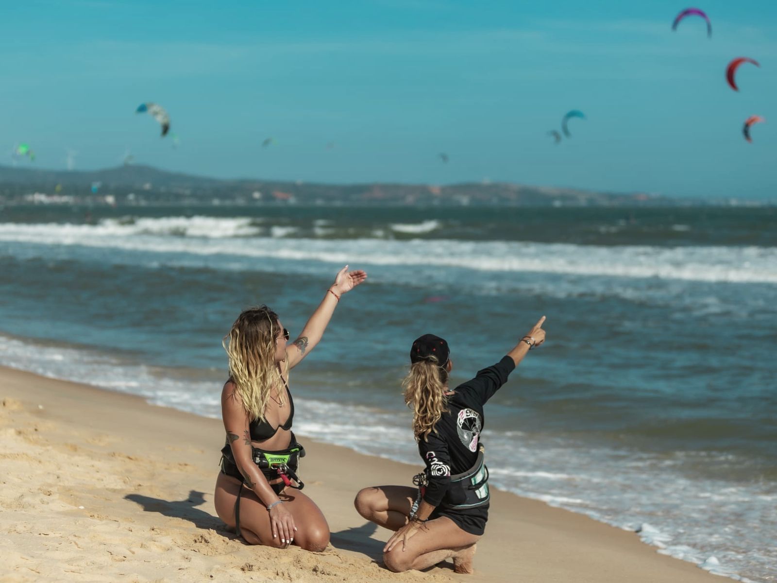 Two C2SKY riders on the beach pointing out kites on the water