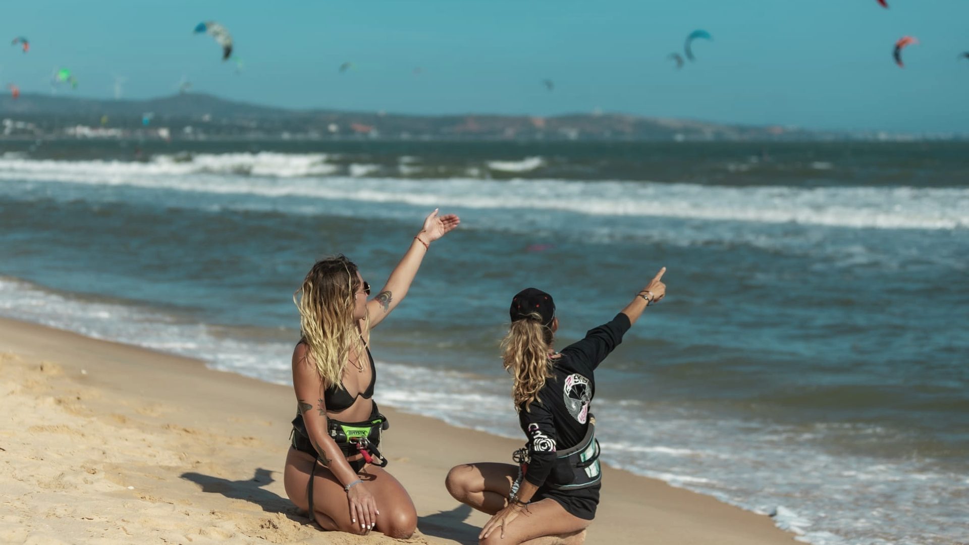 A C2SKY instructor and a student sitting on the sand at Mui Ne, pointing up at the kites.