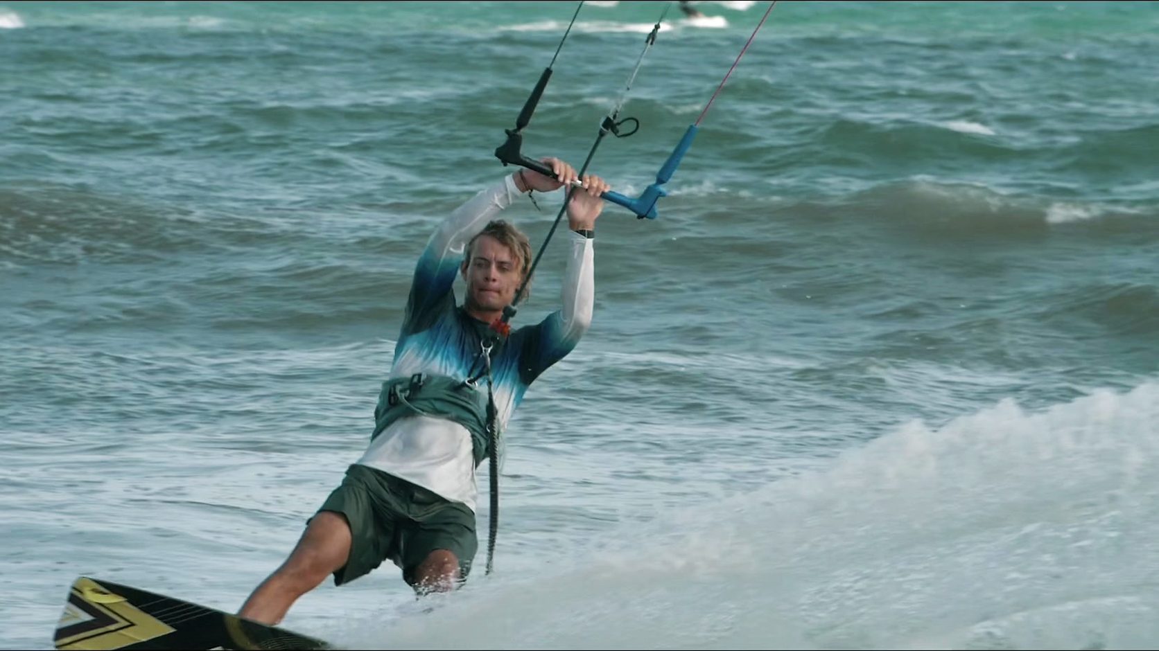 Ein Kitesurfer fährt in Mui Ne, lehnt sich gegen die Bar, Gischt spritzt vom Board.