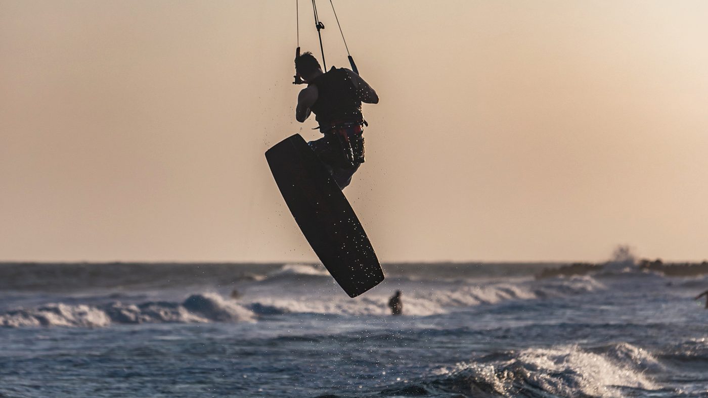 A kitesurfer at the top of a jump, high above the water under a hazy sky.