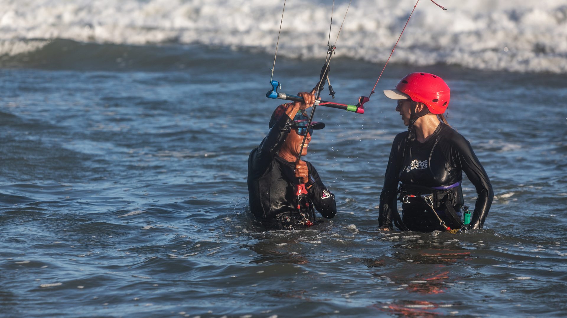 Two people standing together in waist-deep water, working through control-bar handling.