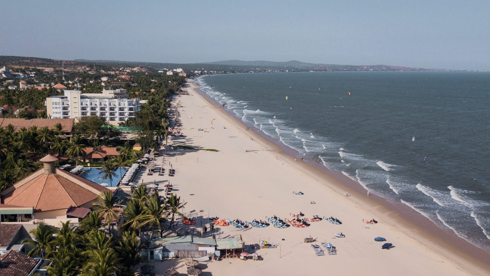 An aerial view along the Mui Ne strip: the beach road, a line of resorts one building deep, the long pale beach and the sea.
