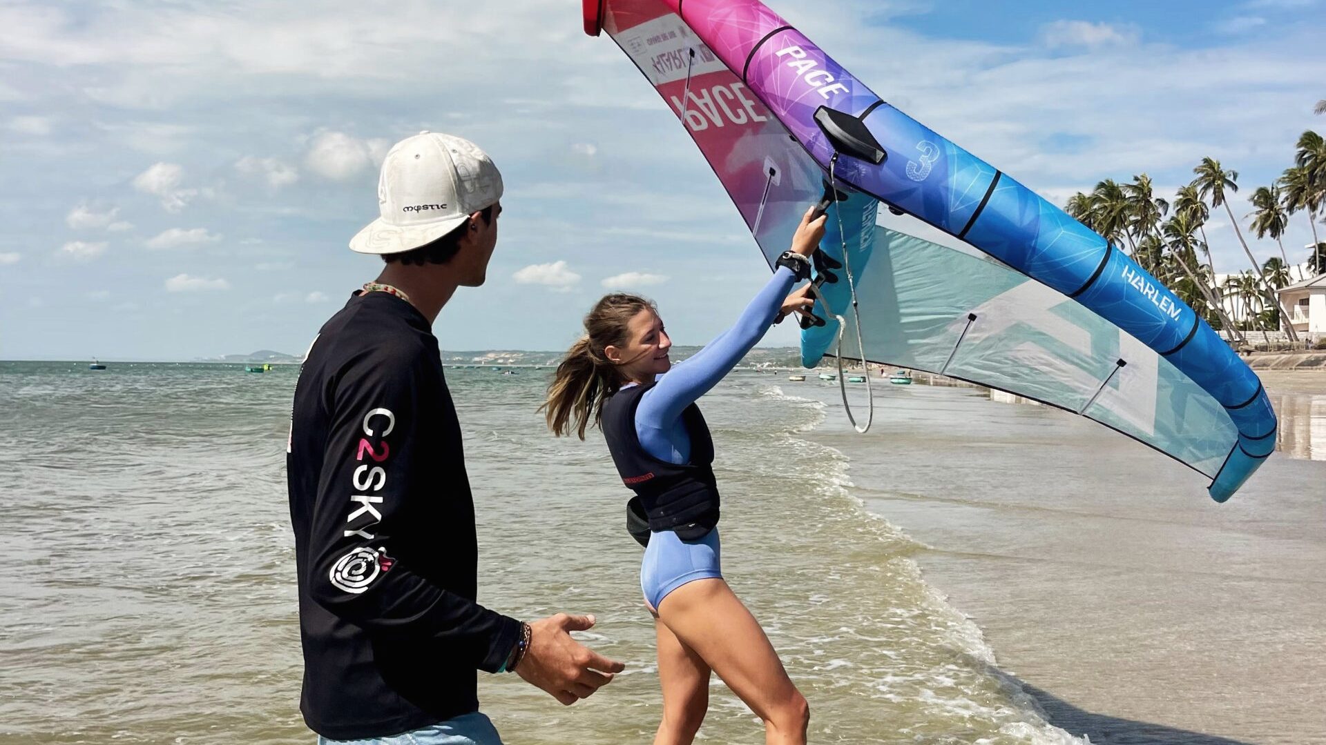 A C2SKY instructor coaching a student who is holding a wing overhead in shallow water at the shoreline.