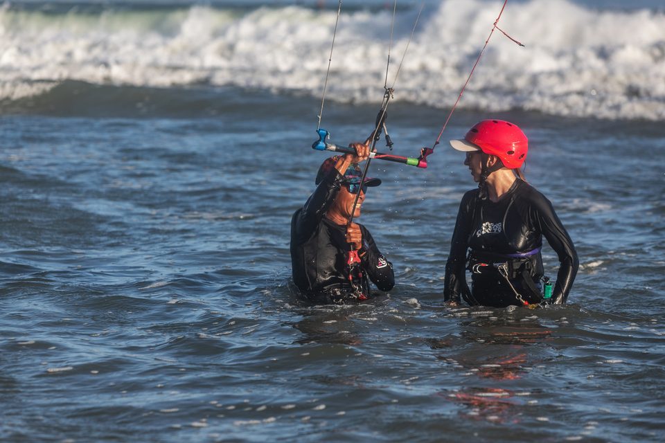 An instructor and a student standing together in waist-deep water at Mui Ne, working through a drill with the kite out of frame.