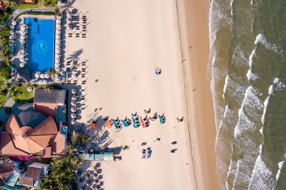 A top-down aerial of a Mui Ne beachfront property: a swimming pool, rows of sun loungers on the sand, and the surf line running along the shore.