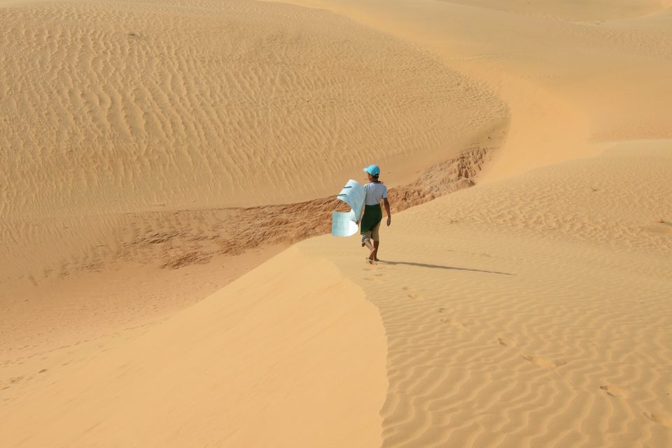 A lone figure walking along the flank of a large, wind-rippled sand dune at Mui Ne.