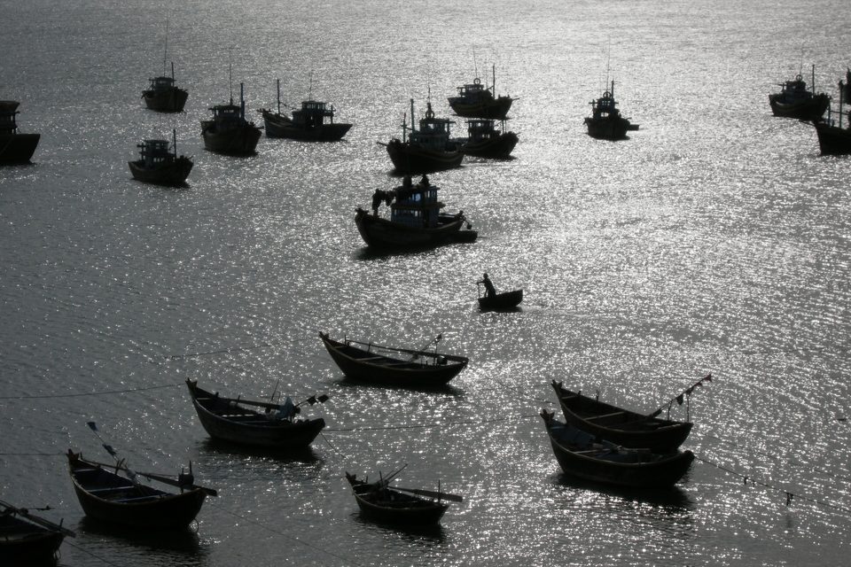 Round-hulled fishing boats at anchor across the harbour at Mui Ne, silhouetted on water lit by a low sun.