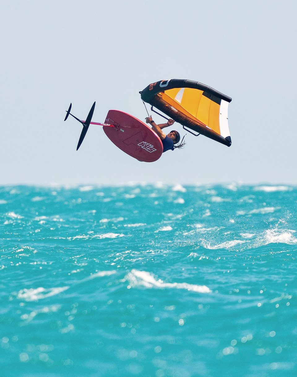 A wingfoiler at Mui Ne clear of the water with the board and foil lifted out, wing held high overhead.